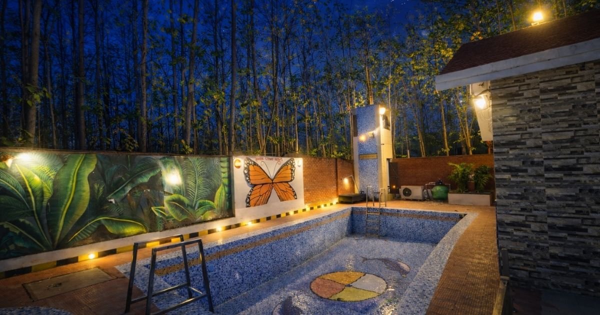 Nighttime view of a tiled rectangular pool in a backyard, with a butterfly mural and lush jungle-themed wall along one side.