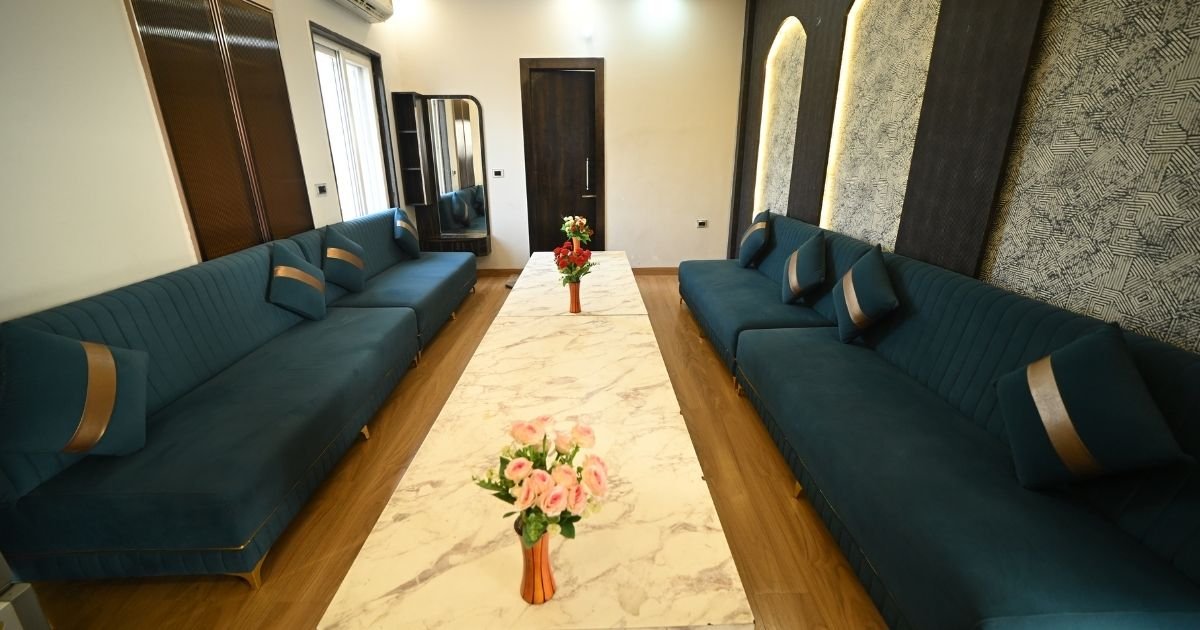 Symmetrical lounge with teal sectional sofas, a long marble coffee table, and pink flower vases.